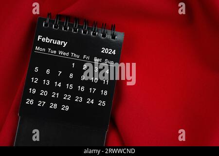Februar 2024 Schwarzer spiralförmiger Desktop-Kalender auf rotem Textil. Stockfoto