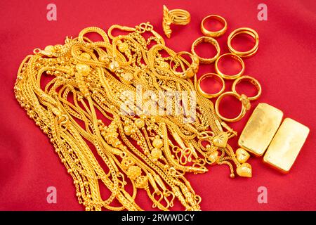 Viele goldene Ketten und Goldbarren auf rotem Samthintergrund. Stockfoto