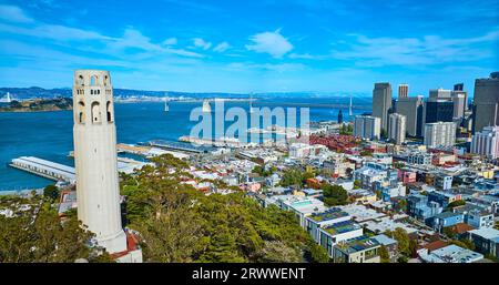 Coit Tower an einem sonnigen Tag mit Wolkenkratzern und Oakland Bay Bridge mit blauem Himmel Stockfoto