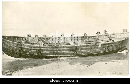 Zehn afrikanische Männer unterstützen ein großes hölzernes Ruderboot am Strand, an einem nicht identifizierten Ort. Stockfoto