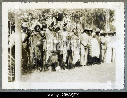 Eine von sieben Bildern mit dem Titel „North Kavirondo Agricultural Show“. Mumias. Januar: 1931.“ Eine Linie afrikanischer Menschen, die verzierte Straußenfedern-Kopfbedeckungen und Schilde tragen, bildet eine Linie, einige stehen und einige auf Ochsen montiert. Stockfoto