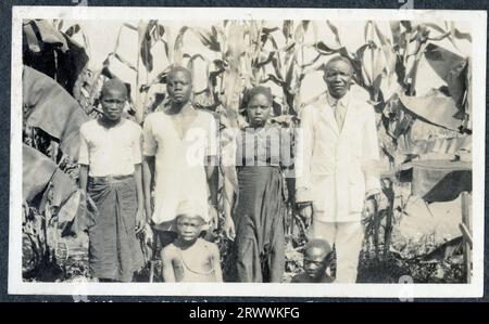 Gruppenfoto einer afrikanischen Familiengruppe, bestehend aus zwei Erwachsenen und vier Kindern, die zwischen Bananenpflanzen stehen. Die Erwachsenen sind elegant in Western-Kleidung gekleidet. Originalhandschrift: Einige Eingeborene Zentralafrikas. Stockfoto