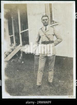 Porträt von Bertie Rand, in Militär- oder Polizeiuniform und auf einem Stock vor einem Wellblechhaus mit Stufen zu einer Veranda gelehnt. Spätere Handschriftenunterschrift: Bertie Rand, N, J&Y g'father. Stockfoto