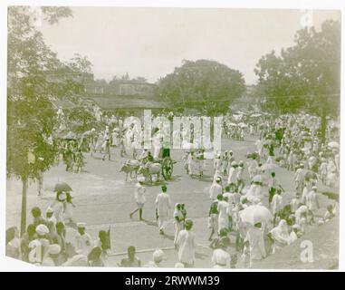 Religiöse Prozession mit geschmückten Wagen inmitten eines großen Festes von traditionell gekleideten Indianern. Bäume säumen den Platz und Gebäude sind im Hintergrund zu sehen. Stockfoto
