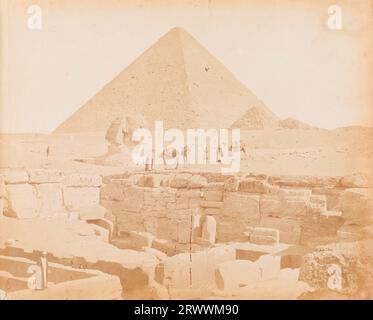 Blick auf die große Sphinx und Pyramiden von Gizeh. Neben der Sphinx sind ägyptische Männer in traditioneller Kleidung, die drei Kamele führen. Im Vordergrund sind die Ruinen der Gizeh-Tempelgräber zu sehen. Beschriftung negativ: 391 Pyramide de CH…[unleserlich]. Stockfoto