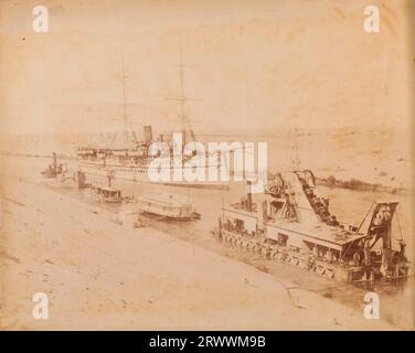 Blick auf ein eintrichtiges Truppenschiff mit drei Masten entlang des Suez-Kanals. Es gibt kleinere Flussschiffe und ein Frachtschiff, das an der Seite des Kanals vertäut ist. Foto von den Brüdern Zangaki. Beschriftung auf negativ: Zangaki. Malabar [unleserlich]. Die handschriftliche Beschriftung lautet: 1893 her Majestys Troopship Malabar in Suez Canal. Stockfoto