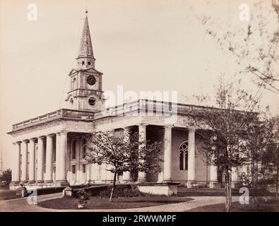 Blick auf die St. John's Church, ein weißes Gebäude im neoklassizistischen Stil mit Kolonnade und Uhrenturm. Job Charnock, der Gründer von Calcutta, ist hier begraben. Die Bildunterschrift lautet: St John's Calcutta, ehemals Kathedrale. "Job Charnock" ist hier begraben. Stockfoto