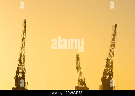 Drei alte Schiffskraniche in Silhouette in goldenem Licht am späten Nachmittag in Fremantle, Western Australia Stockfoto