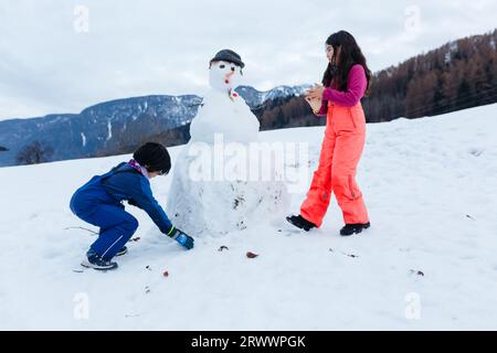 Zwei Kinder machen Schneemann auf dem schneebedeckten Berg Stockfoto