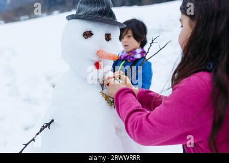 Nahansicht von zwei Kindern, die auf dem schneebedeckten Berg Schneemann machen Stockfoto