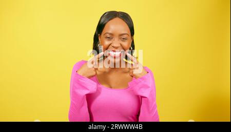 Schöne junge Frau zeigt auf Lächeln, weiße Zähne, glücklich im gelben Studio Stockfoto