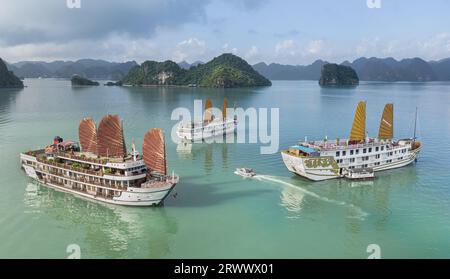 Die Landschaft der Halong-Bucht aus der Vogelperspektive, Hạ lange Kreuzfahrtschiffe, die zwischen Kalksteinfelsen aus türkisfarbenem Wasser ankern, Vietnam-Junks mit Segeln Stockfoto