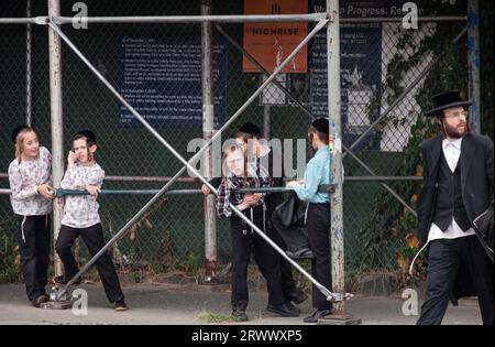 Eine Straßenszene in einem chassidisch-jüdischen Viertel. Schuljungen warten auf ihren Bus und ein Mann geht in den Tempel. Auf der Lee Avenue in Williamsburg. Stockfoto