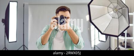 Junger männlicher Fotograf, der im Studio arbeitet und Fotos mit seiner professionellen Kamera macht Stockfoto