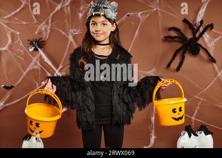 Smiley Kid in Wolfsmaske mit zwei Kürbiseimern auf braunem Hintergrund mit Netzen, Halloween, Nahaufnahme Stockfoto