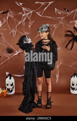Teenager-Mädchen mit Halloween-Spielzeug auf braunem Hintergrund mit Spinnen, Netz und Laternen, Halloween Stockfoto