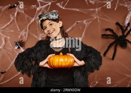 Smiley Preteen Girl, das Kürbis in den Händen hält, auf braunem Hintergrund, Halloween-Konzept Stockfoto