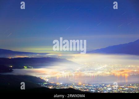 Wolkenmeer über den Lichtern der Stadt Suwa und Sternenhimmel vom Takabotchi Plateau Stockfoto