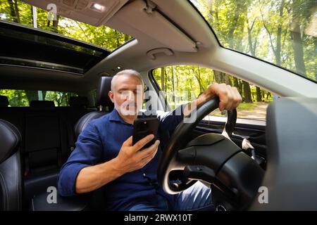 Zufriedener junger Mann mit Telefon im Auto Stockfoto