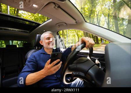 Zufriedener junger Mann mit Telefon im Auto Stockfoto