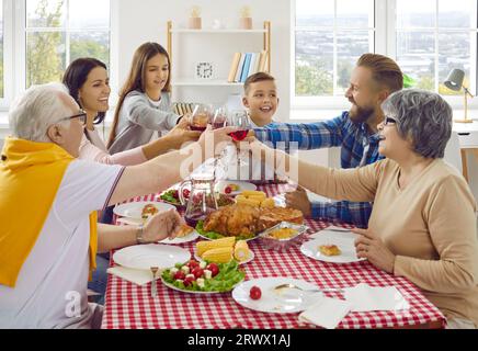 Fröhlich freundliche, generationenübergreifende Familie, die während der Thanksgiving-Feier Weingläser klatscht. Stockfoto