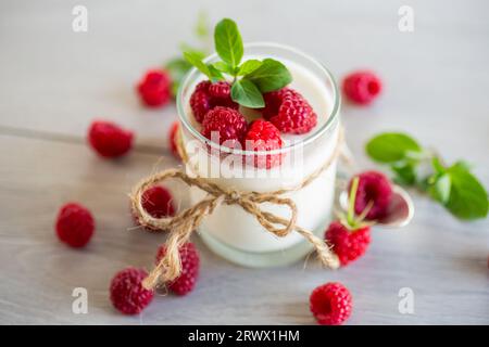Gekochter hausgemachter Joghurt mit Reifen roten Himbeeren in einem Glas auf einem Holztisch. Stockfoto