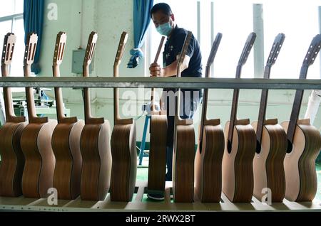 (230921) -- GUIYANG, 21. September 2023 (Xinhua) -- Ein Arbeiter stellt eine halbfertige Gitarre auf ein Regal in einer Werkstatt des Zheng'an Guitar Culture Industry Park im Kreis Zheng'an, Provinz Guizhou im Südwesten Chinas, 25. März 2020. Nach mehr als 200 aufwändigen und langwierigen Herstellungsverfahren kommen exquisit gefertigte Gitarren als charakteristische Produkte des Zheng'an County in der südwestlichen chinesischen Provinz Guizhou heraus. Diese Kunstwerke werden dann über die China-Europa-Güterzüge, den Wassertransport und andere Mittel in die Welt verteilt. MIT "Economic Watch: Chinesische Gitarrenproduktion" Stockfoto