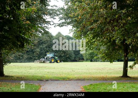 Ein Auftragnehmer des rates, der mit einem Traktor Grasschneider in einem großen öffentlichen Park und auf einem Spielfeld Gras schneidet. Der Grasschnitt ist zurückgeblieben Stockfoto