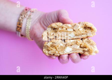Eine Frau, die einen zerbrochenen hausgemachten Erdnussbutter-Chip-Keks im New Yorker Stil hält. Es ist ein großer Keks mit einer knusprigen äußeren Kruste und einer weichen Mitte. Stockfoto