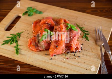 Frische große Stücke gesalzener roter Fische mit Gewürzen und Kräutern auf einem Holzbrett. Stockfoto