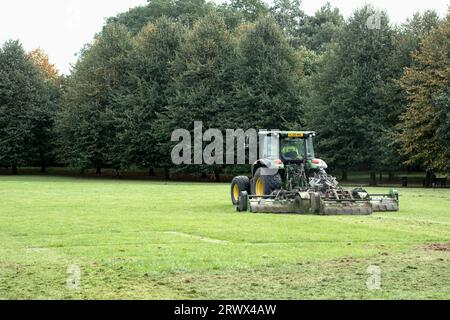 Ein Auftragnehmer des rates, der mit einem Traktor Grasschneider in einem großen öffentlichen Park und auf einem Spielfeld Gras schneidet. Der Grasschnitt ist zurückgeblieben Stockfoto