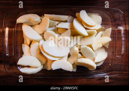 Geschälte und in Scheiben geschnittene Äpfel in einer Klarglas-Auflaufform auf einem Holztisch Stockfoto
