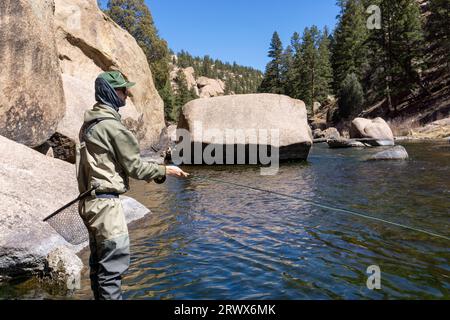 Mann, der in den Bergen im Fluss steht und Fliegenfischer wirft Stockfoto