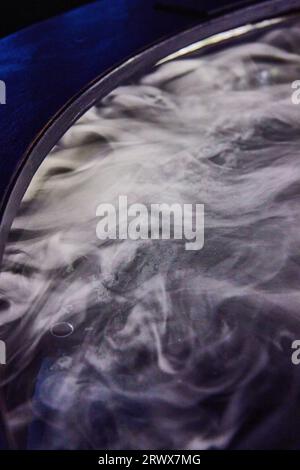 Weißer Nebel, der in einem schwarzen, kreisförmigen Kessel wie ein Behälter herumwirbelt Stockfoto