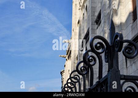 Zwei Wasserspeier an der Seite der Basilika Sacré Coeur über einem schwarzen geschwungenen schmiedeeisernen Zaun in Montmartre, Paris, Frankreich Stockfoto