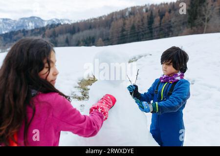 Nahaufnahme von zwei Mädchen, die auf dem schneebedeckten Berg Schneemann machen Stockfoto