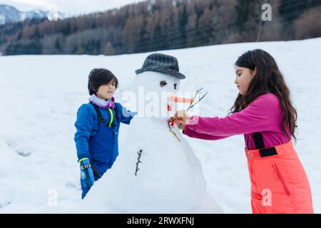 Zwei Mädchen machen Schneemann auf dem schneebedeckten Berg Stockfoto