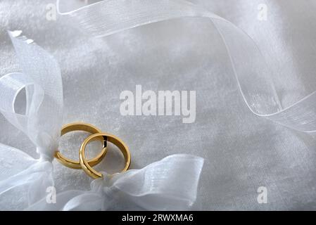 Zwei goldene Ringe, gebunden mit Band auf weißem Tuch. Draufsicht. Stockfoto