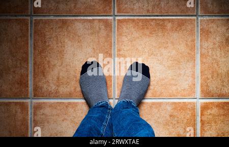 Bild von oben von zwei Füßen mit gestreiften Socken auf einem gefliesten Boden in warmen Tönen. Selfie-Konzept. Stockfoto