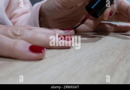 Nahaufnahme der Hände einer Reifen Frau, die ihre Nägel dunkelrot mit geringer Feldtiefe malte. Stockfoto