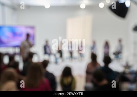 Hintergrund nicht erkennbarer Personen, die mit dem Rücken zur Kamera stehen und der Bühne zugewandt sind, auf der die Lautsprecher sprechen. Geschäftsereignis. Hochwertige Fotos Stockfoto