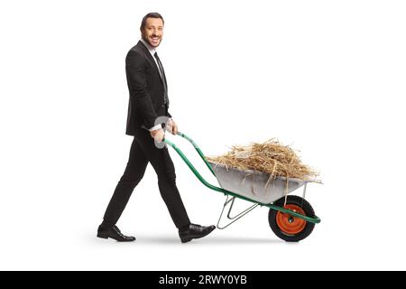 Profilaufnahme in voller Länge eines Geschäftsmannes, der mit Heu in einer Schubkarre auf weißem Hintergrund läuft Stockfoto