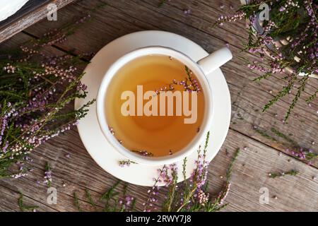 Heidekraut- oder Calluna vulgaris-Tee in einer weißen Keramikschale mit frisch blühender Pflanze, Blick von oben Stockfoto