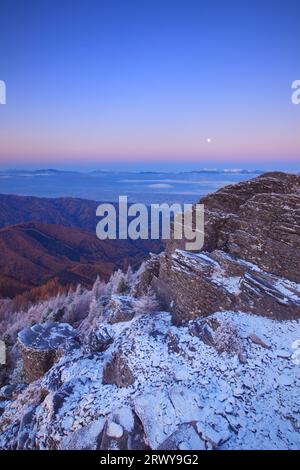 The rocky ridge of Oogahana with fresh snow, the moon in the morning, and a distant view of the Hotaka mountain range and other peaks Stock Photo