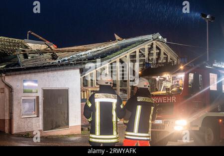 Nusbaum, Deutschland. September 2023. Freiwillige Feuerwehrleute stehen vor einem Bauernhof, dessen Dach fehlt. Schwere Winde haben zahlreiche Dächer im Dorf Bitburg-Prüm in der Eifel bedeckt. Ein weiterer Schwerpunkt der Operation sei die Ortsgemeinde Hüttingen-Lahr, sagte er. "Es soll dort ein Erdrutsch gegeben haben." Quelle: Harald Tittel/dpa/Alamy Live News Stockfoto