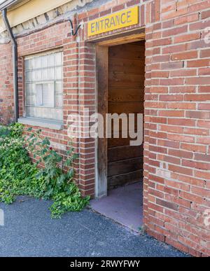 DAS EINGANGSSCHILD an der offenen Tür des Geschäftsgebäudes aus rotem Backstein zeigt eine dunkle Holzausstattung. Die alte Ziegelfassade hat ein Glasziegelwandfenster. AI verwendet Stockfoto