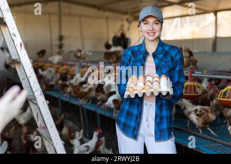 Junge Landwirtin in Europa, die in der Geflügelzucht einen Karton voller frischer Hühnereier hält Stockfoto