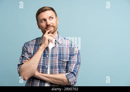 Nachdenklicher, nachdenklicher Mann, der das Kinn berührt und auf dem Studiohintergrund nach oben schaut, um Werbung zu machen Stockfoto