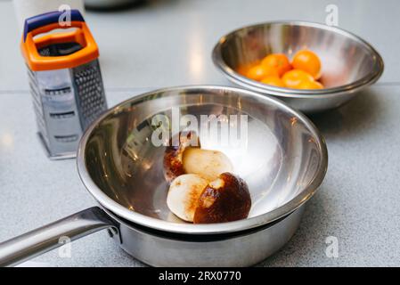 Ein Set Küchenutensilien vor dem Kochen, Edelstahlschalen, eine Reibe und aufgetaute Steinpilze, eine Pfanne aus Metall auf einem Küchentisch. Stockfoto