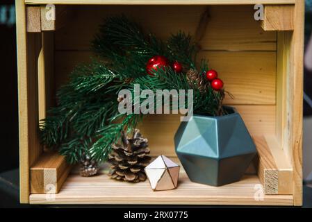 Weihnachtsdekoration in Form eines Weihnachtsbaumzweigs auf einem Holzregal mit geometrischer Figur und einem Tannenzapfen Stockfoto